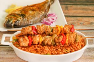 Close-up of flavorful Nigerian jollof rice with grilled chicken skewers and roasted fish.